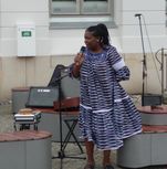 Eine Schwarze Frau in einem gemusterten Kleid spricht ins Mikrofon.