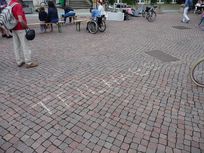 Das Wort Teilhabe steht mit Kreide geschrieben auf dem Boden. Im Hintergrund ist unter anderem ein Mensch im Rollstuhl zu sehen.