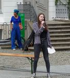 Eine junge weiße Frau in schwarzer Hose und kariertem Hemd hält einen Zettel in der Hand und spricht ins Mikrofon.