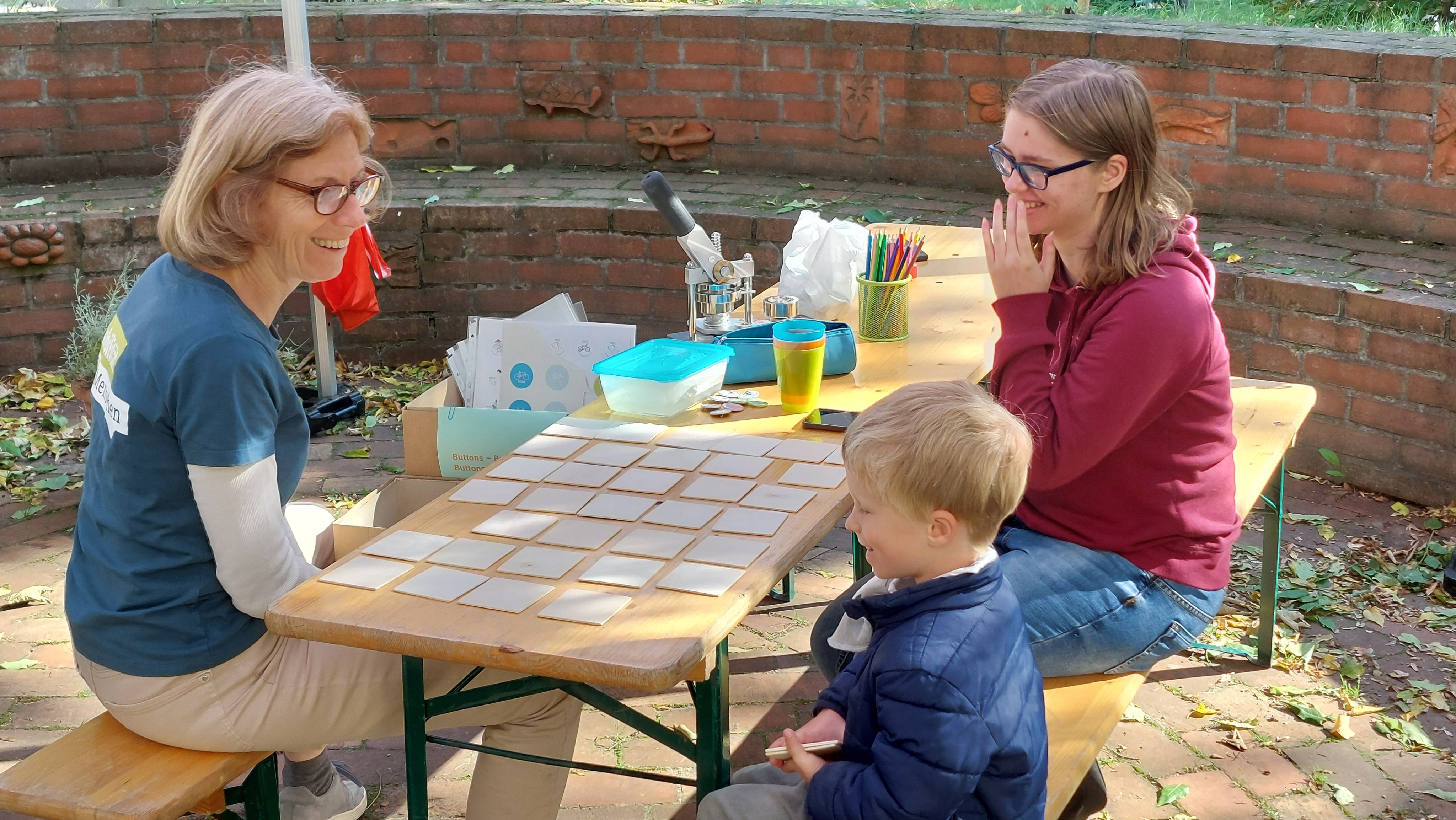 Zwei VCD Mitglieder spielen mit einem Kind ein Verkehrsmemory.